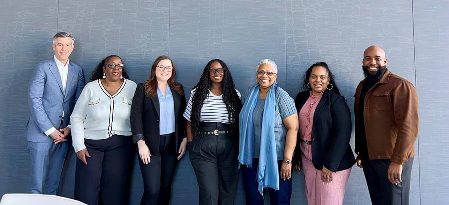 5 women and 2 men smiling for a photo together.